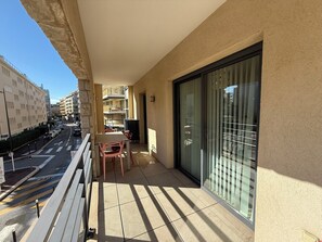 Un balcon avec une table et des chaises, une porte vitrée et une vue sur la rue et les immeubles.