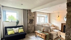 Een woonkamer met een zwarte bank, een beige bank, een houten salontafel en een vloerkleed met een patroon.