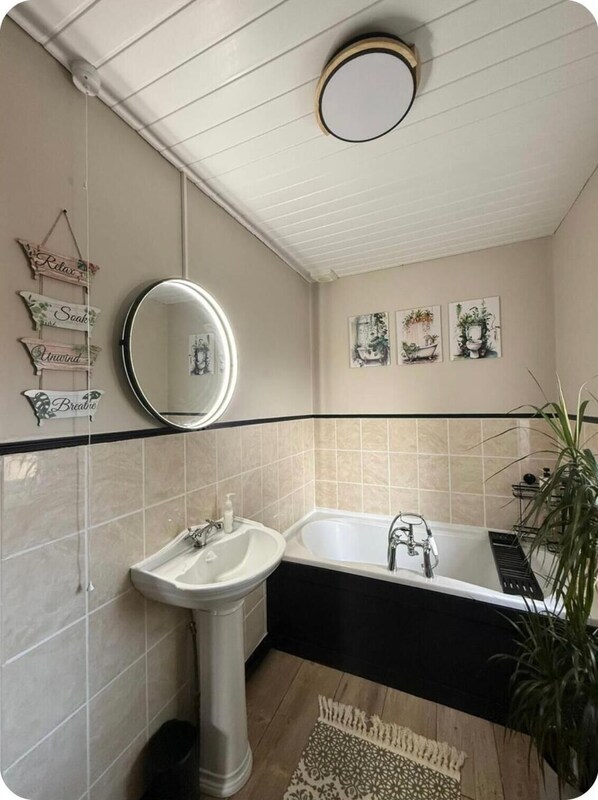 A bathroom with a pedestal sink, a freestanding bathtub, and a round mirror. There are wall-mounted signs with words like "Relax" and "Breathe."
