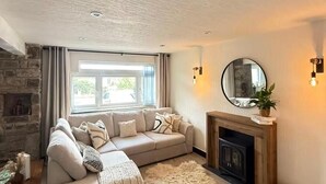 Een gezellige woonkamer met een stenen openhaard, een grote beigekleurige bank en een zacht tapijt.