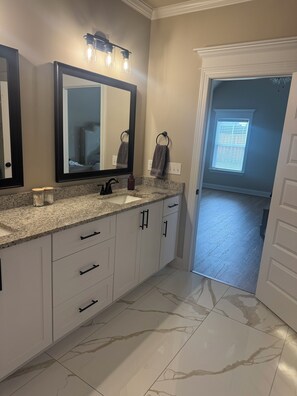 A bathroom with a granite countertop, white cabinets, a large mirror, and a vanity light fixture. - 2026 Masters Rental - 11 Miles from Augusta National (Evans)
