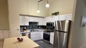 A modern kitchen with white cabinets, stainless steel appliances, a wooden table, and a patterned rug. - Relaxed Desert Stay - 3BR/2BA Tucson Home - Furnished & Spacious (Tucson)