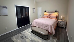 A bedroom with a bed, a bench, a nightstand, a ceiling fan, a door, and a wall-mounted light fixture. - Relaxed Desert Stay - 3BR/2BA Tucson Home - Furnished & Spacious (Tucson)