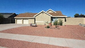 A residential house with a garage, a small patio area with a bench, and a landscaped garden with mulch and small plants. - Relaxed Desert Stay - 3BR/2BA Tucson Home - Furnished & Spacious (Tucson)