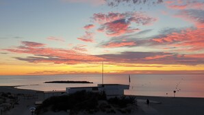 En strandutsikt med en solnedgång, ett lugnt hav och en liten ö.