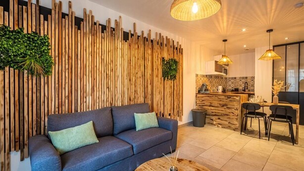 Een moderne woonkamer met een donkerblauwe bank, een ronde houten salontafel en een verticale houten wanddecoratie.