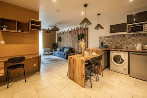 Una cucina compatta con lavatrice, un'area pranzo con tavolo in legno e un divano sullo sfondo.