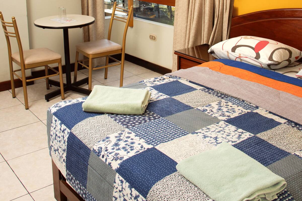 Una habitación de hotel con cama, una mesita, dos sillas y una ventana con cortinas.
