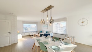 Un comedor moderno con una mesa blanca dispuesta para cuatro personas, rodeada de sillas verdes y blancas.