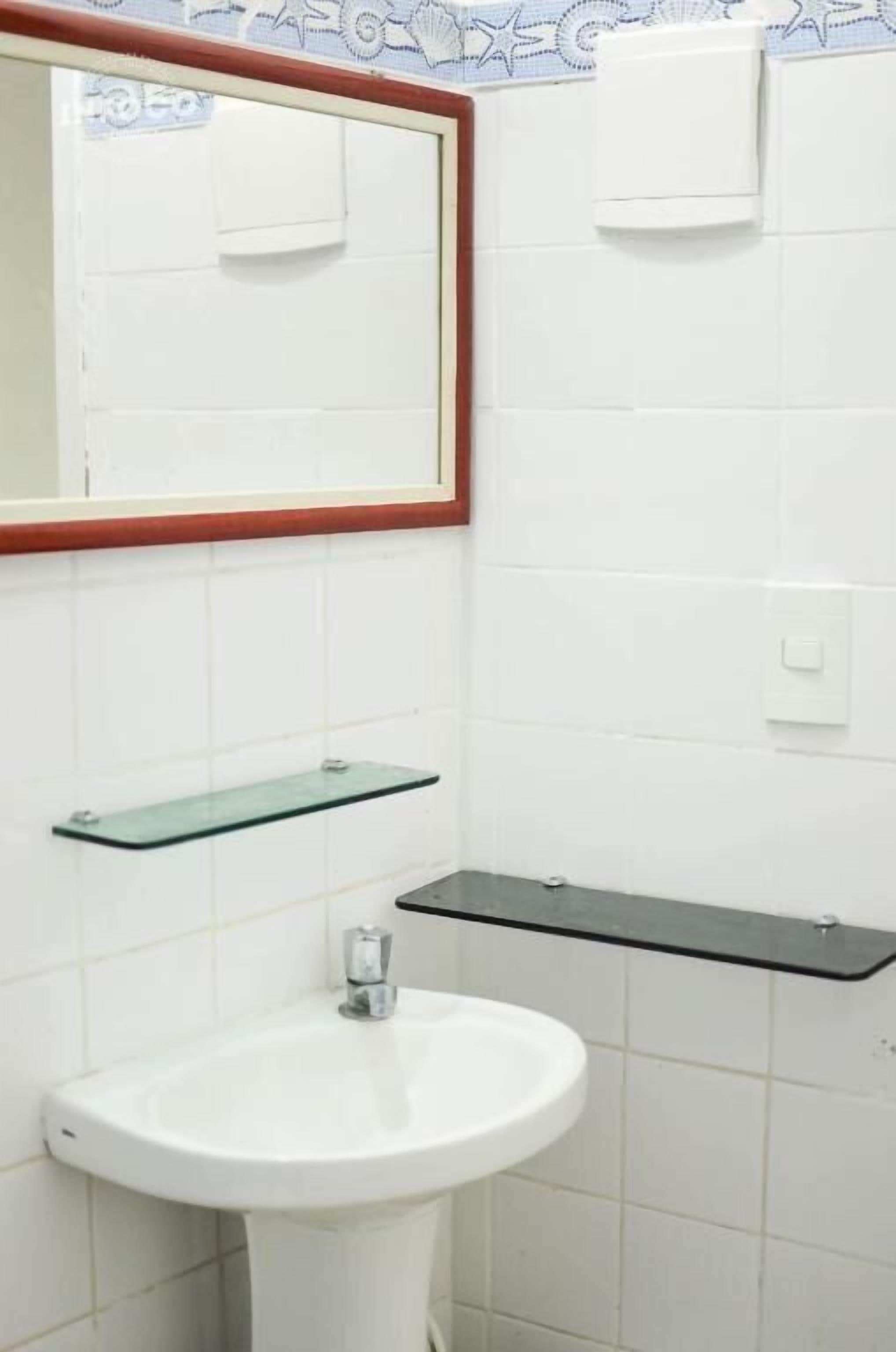 Un baño con un lavamanos blanco, un estante de vidrio y un espejo con marco de madera.