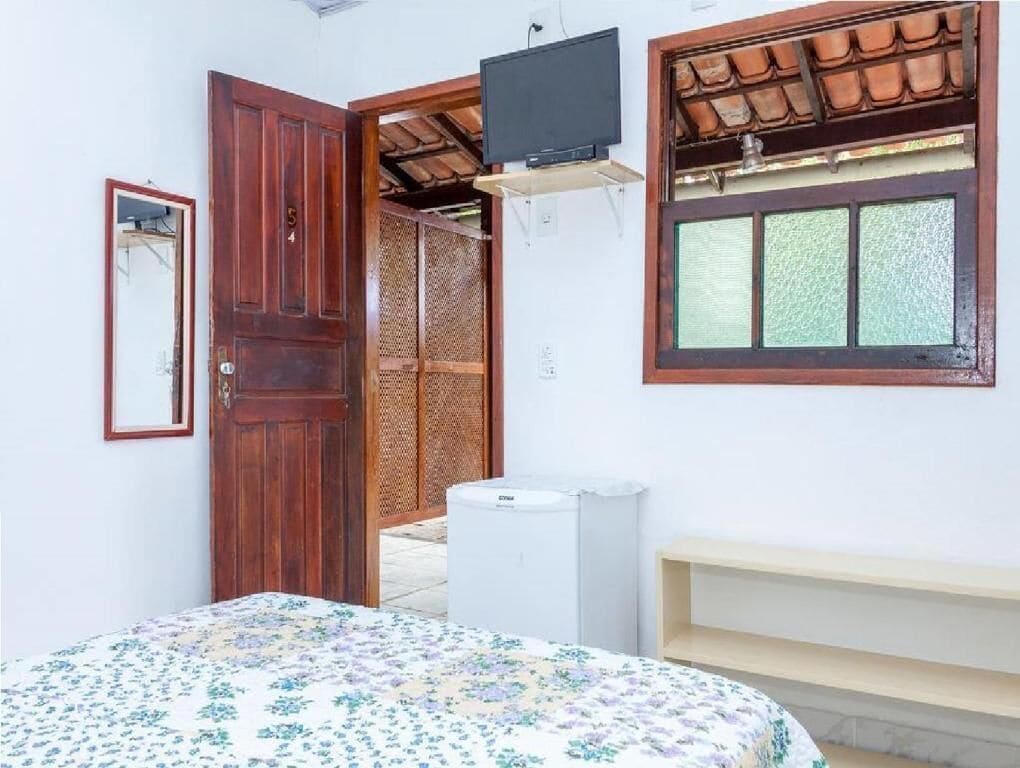 Quarto com uma cama, porta de madeira, televisão e janela com vista.