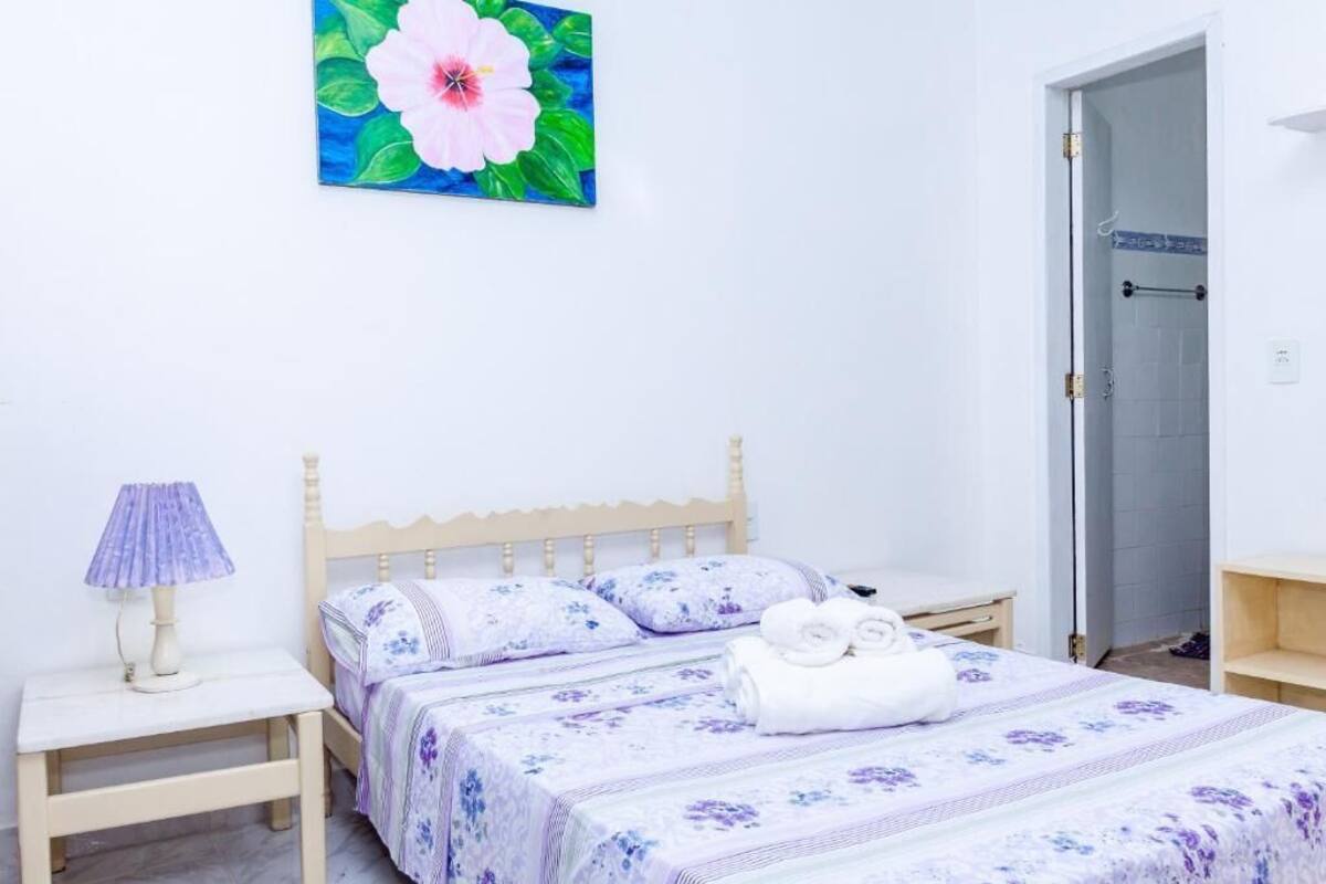 Un dormitorio con una cama de madera, una mesita de noche con lámpara, una puerta de baño y un cuadro grande con motivos florales en la pared.