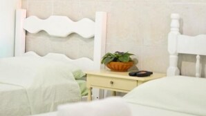 A hotel room with two beds, a white headboard, a painting of sunflowers, and a small table with a plant. - Pousada Sossego (Buzios)