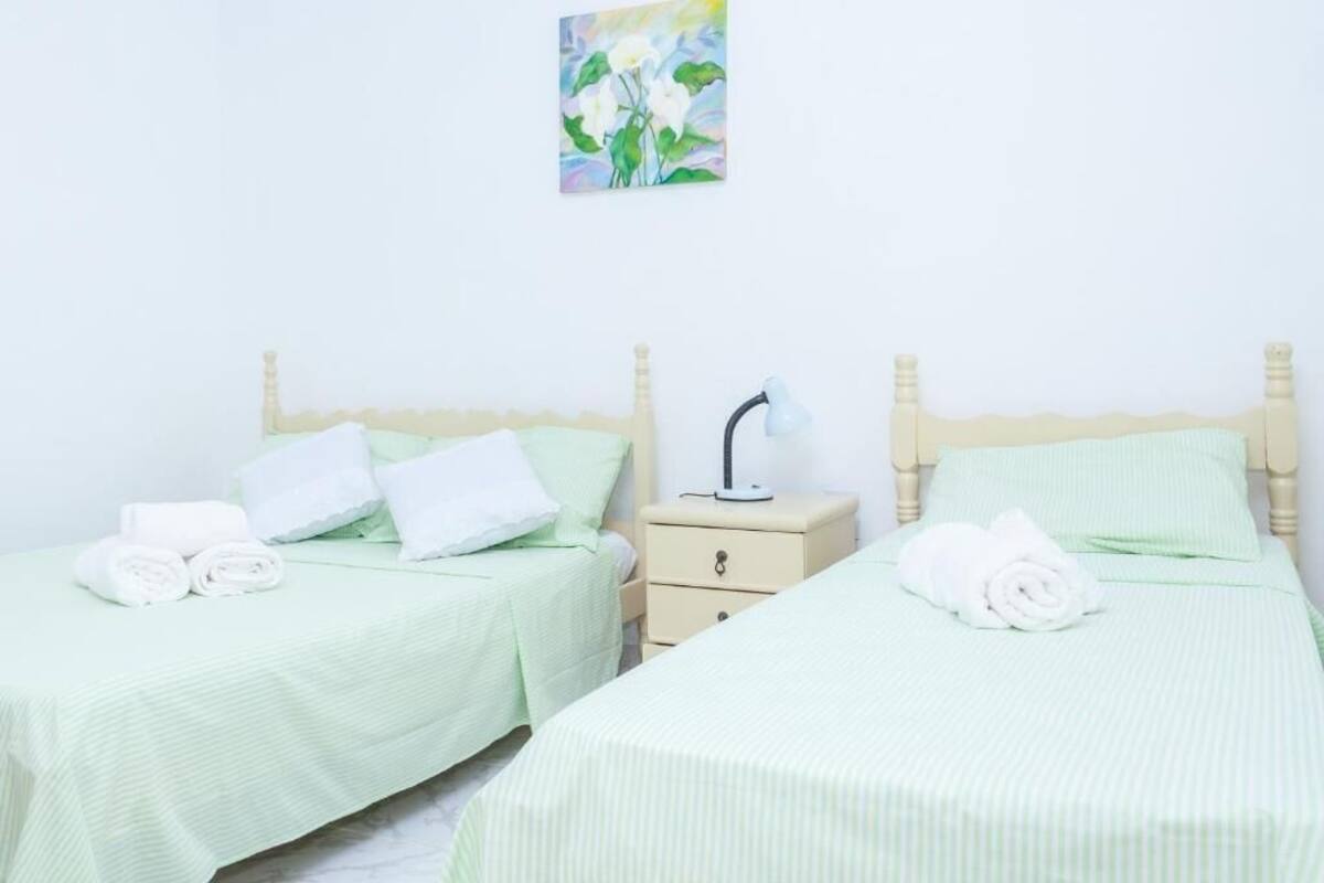 Habitación de hotel con dos camas, cada una con cubrecama verde y almohadas blancas. Hay una mesita de noche con una lámpara entre las camas.