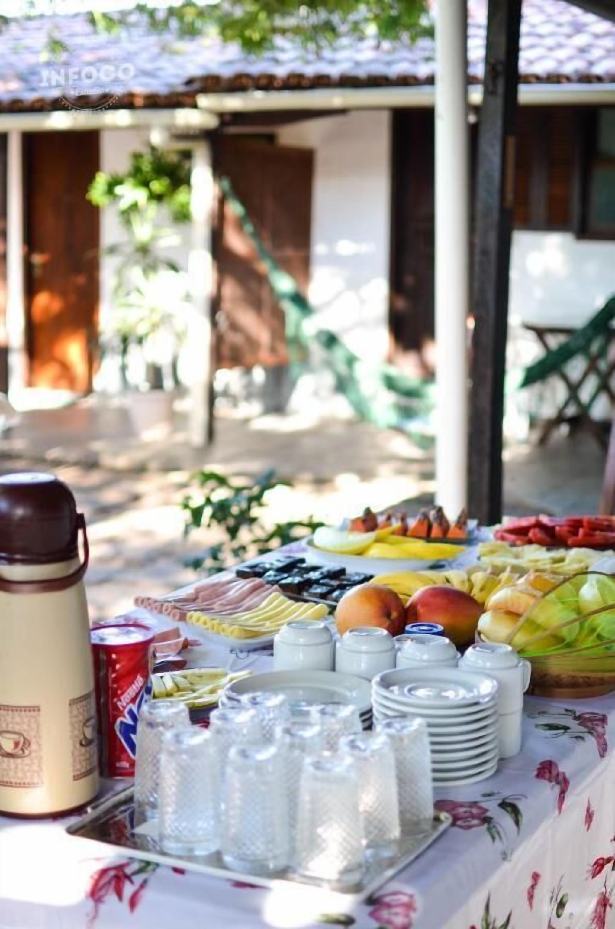 Une table dressée à l’extérieur, avec différents fruits, des condiments et un thermos.