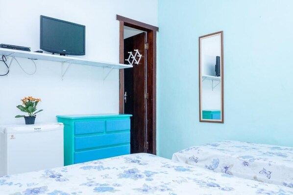 Une chambre à coucher avec un lit, une commode, un téléviseur posé sur une étagère et une porte ornée de motifs géométriques.