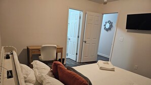 A hotel room with a bed, a desk, a chair, and a television on the wall. - Oxford Cottage (Oxford)