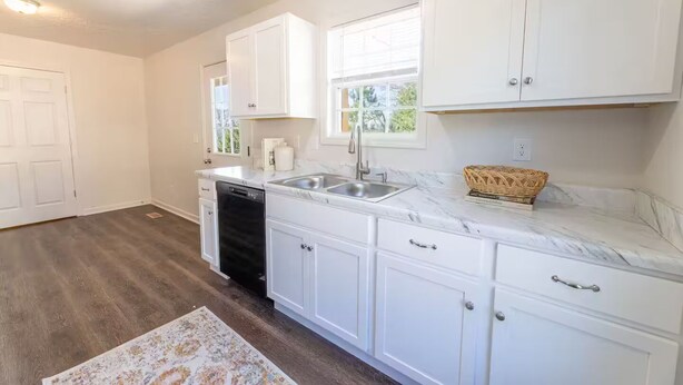 A kitchen with white cabinets, a marble countertop, a dishwasher, and a window with blinds. - Oxford Cottage (Oxford)