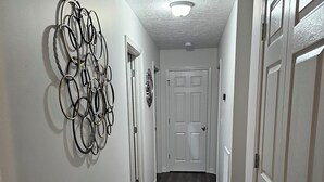 A hallway with a wooden floor, white walls, and a ceiling light. There are two doors on the right and a wall decoration on the left. - Oxford Cottage (Oxford)
