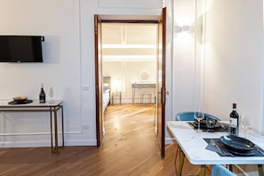 A modern hotel room with a wooden floor, a dining table set with plates, glasses, and a bottle, and a TV mounted on the wall. - Elegant apartment 100 Mt from Trevi Fountain for couples and families (Roma)
