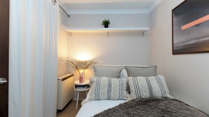 Ein Schlafzimmer mit einem Bett, einem Nachttisch, einer Lampe und einer kleinen Pflanze auf einem Regal.