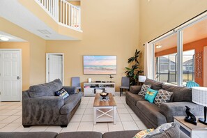 A spacious living room with two grey sofas, a wooden coffee table, and a large window with a view of the outdoors. - Family Disney Retreat • Pool • Spa • Game Rooms • Resort Amenities (Kissimmee)