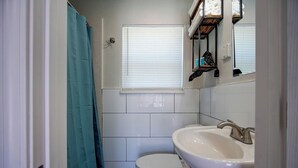 Een kleine badkamer met toilet, wastafel en een raam met zonwering.