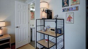 Um corredor com porta branca, luminária, prateleira com garrafas de água e arte na parede, incluindo uma placa com a inscrição 'Stay Wild Moon Child'.