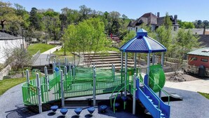 Um parquinho com um escorregador azul, estruturas de escalada verdes e uma área de recreação coberta.