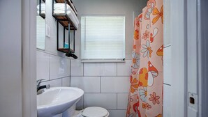 Casa de banho pequena com lavatório branco, sanita e cortina de chuveiro com padrão floral.