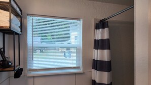 A bathroom with a window, a shower curtain, and a towel rack. - The Bambino at PWC (Hot Springs)