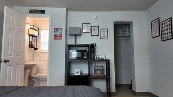 A bedroom with a bed, a bathroom with a toilet and sink, a microwave, a coffee maker, and framed baseball memorabilia on the wall.