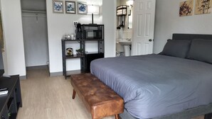 Een slaapkamer met een bed, een bankje, een kledingkast en een bureau met een lamp.