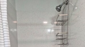 A shower with a metal rack, a showerhead, and a control knob. - The Boardwalk at PWC (Hot Springs)
