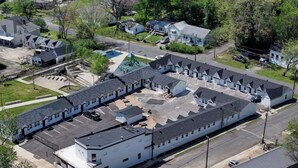 A large, multi-story building with a central courtyard, surrounded by parking spaces and residential houses. - The Boardwalk at PWC (Hot Springs)