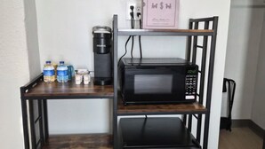 A kitchenette with a microwave, refrigerator, and coffee maker on a metal shelf unit. - The Boardwalk at PWC (Hot Springs)