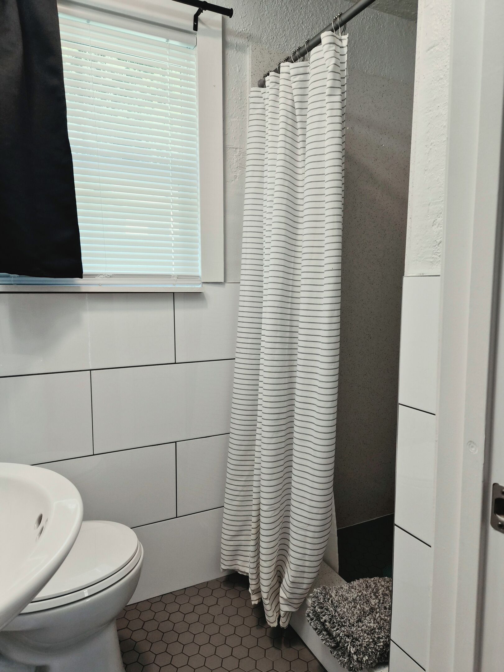 A bathroom with a toilet, a shower curtain, and a window with blinds.
