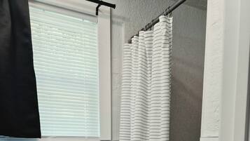 A bathroom with a toilet, a shower curtain, and a window with blinds.