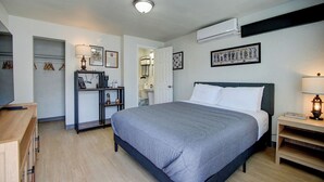A hotel room with a large bed, bedside tables, a desk, and an air conditioning unit. - The Gettysburg at PWC (Hot Springs)