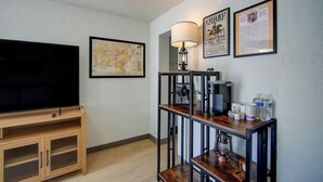 A room with a TV, a map, a coffee machine, and a framed poster on the wall. - The Gettysburg at PWC (Hot Springs)