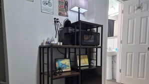 Une étagère en métal noir, avec un micro-ondes posé dessus, un tableau encadré et une petite maquette de vélo.