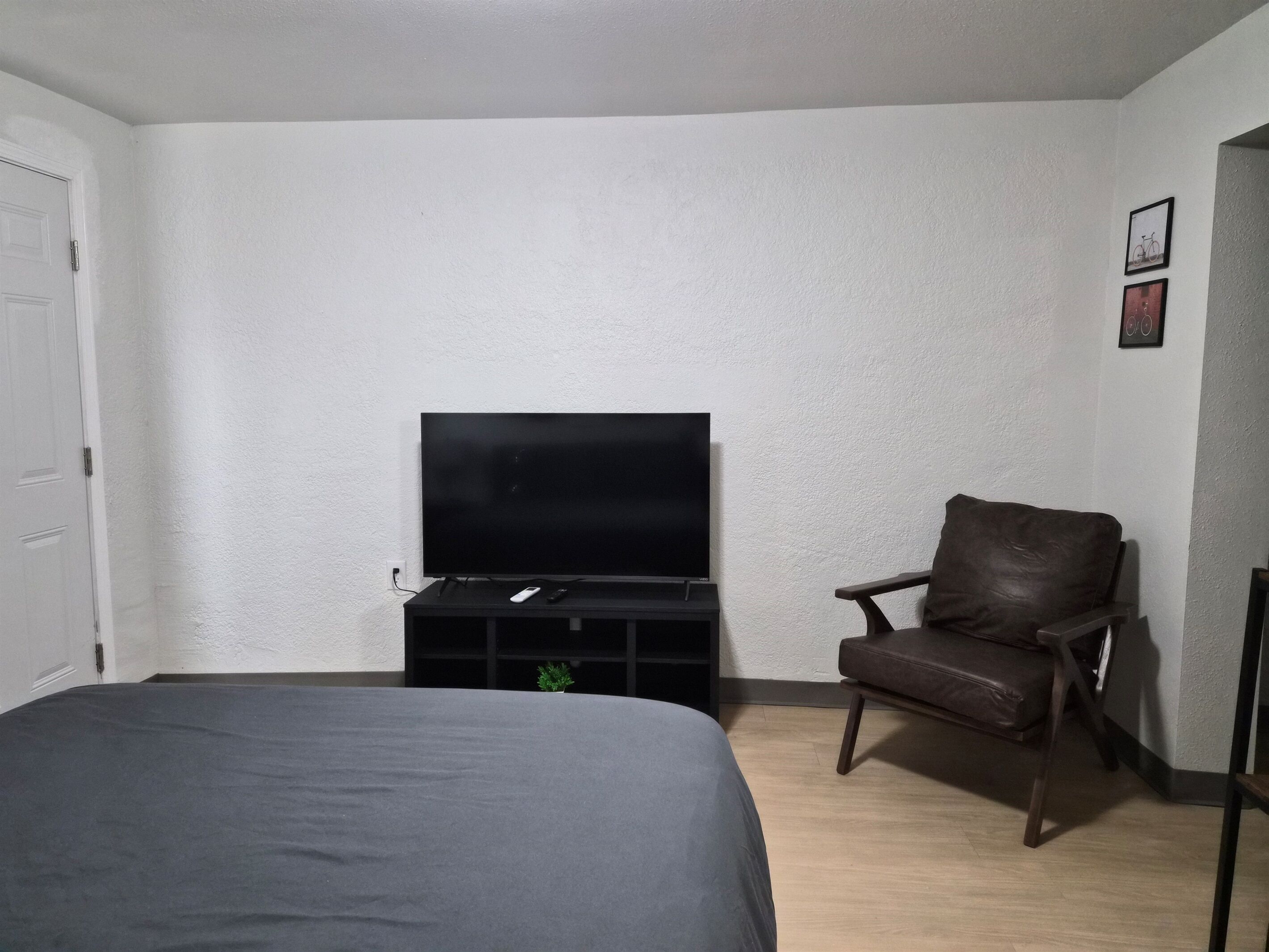 Een slaapkamer met een bed, een televisie op een standaard, een lederen fauteuil en een kleine plant.