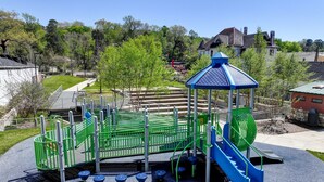 Une aire de jeux avec des structures colorées, vertes et bleues, comprenant un toboggan et une zone d’escalade, le tout entouré d’une clôture.