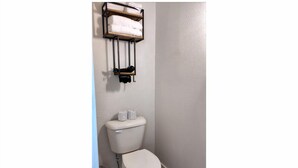 A bathroom with a toilet, a towel rack, and a trash bin. - The Capone at PWC (Hot Springs)