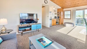 A modern living room with a flat-screen TV, a coffee table with a decorative tray, a sofa, and a dining area with a kitchen in the background. - Family fun in this spacious 3 bedroom home with game room and ocean views (Brookings)