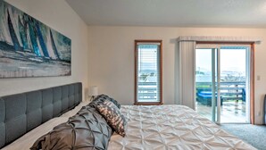A modern hotel room with a large bed, a painting on the wall, and a view of the outdoors through a sliding glass door. - Family fun in this spacious 3 bedroom home with game room and ocean views (Brookings)