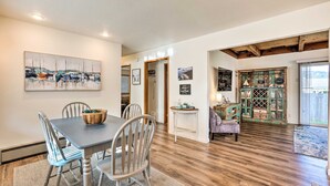 A dining area with a wooden table and chairs, a painting on the wall, and a view of the living room with a wooden floor and a bookshelf. - Family fun in this spacious 3 bedroom home with game room and ocean views (Brookings)