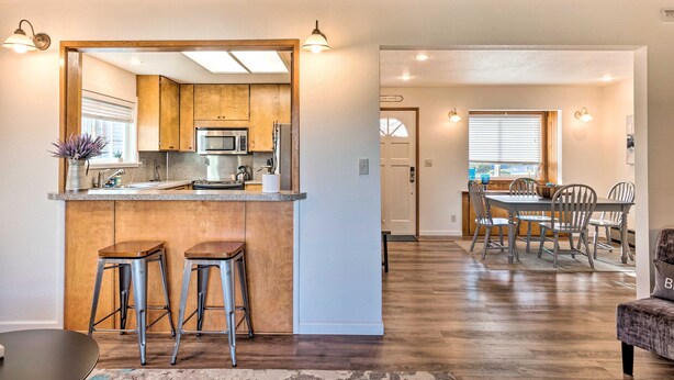 A modern kitchen with wooden cabinets, a bar stool, and a dining area with a table and chairs. - Family fun in this spacious 3 bedroom home with game room and ocean views (Brookings)