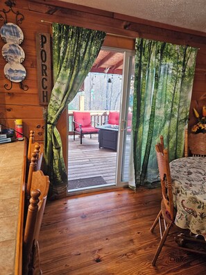 A wooden interior with a sliding glass door leading to an outdoor patio area with red chairs and a table. - Sleepy Meadows a Quiet 3 bedroom cabin retreat in the foothills of Rutherfordton (Rutherfordton)