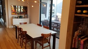 En matplats med ett vitt bord och trästolar, en bokhylla fylld med böcker och ett stort fönster med utsikt över omgivningen.